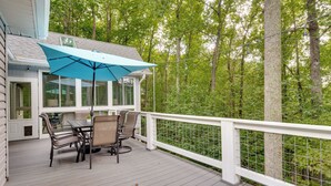 Eine überdachte Terrasse im Freien mit Tisch und Stühlen, umgeben von einem weißen Geländer und Blick auf einen Wald.