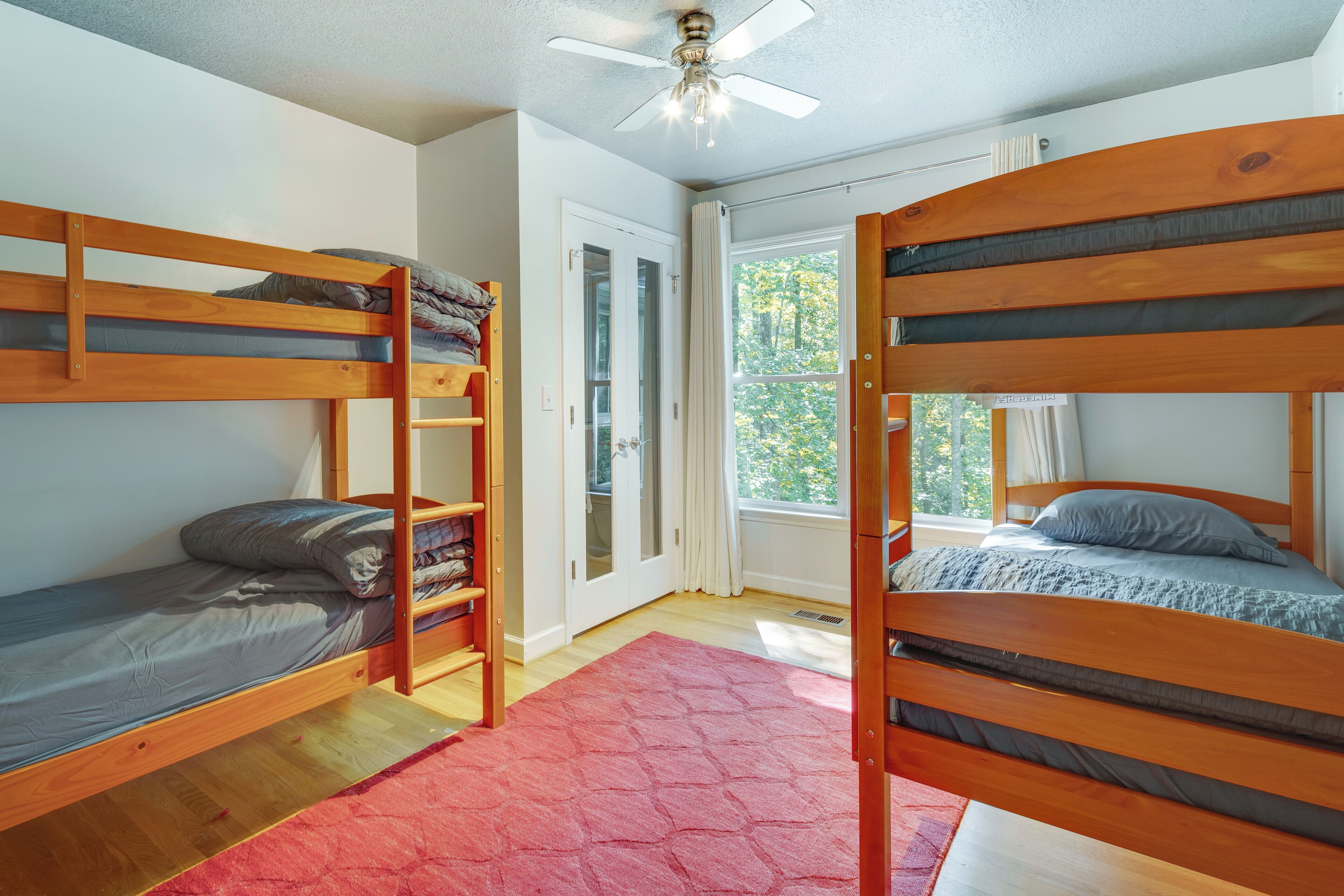 A room with two bunk beds, a ceiling fan, a window with curtains, and a red rug.