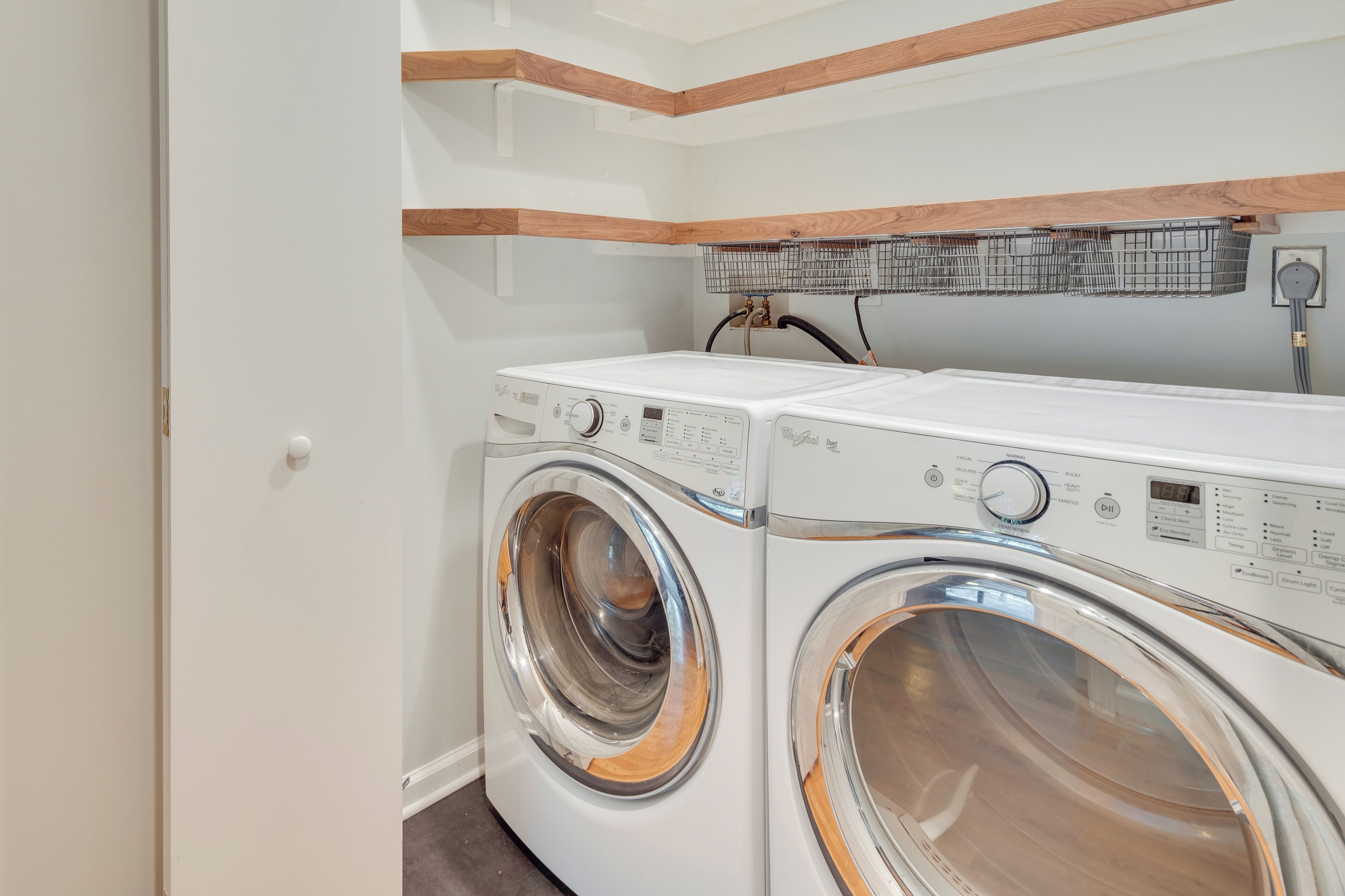 A laundry room with two front-loading washing machines, wooden beams on the ceiling, and a power outlet on the wall.