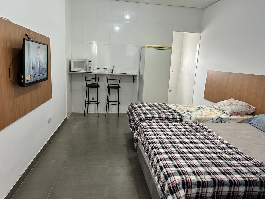 Une chambre d’hôtel de taille réduite, comprenant un lit, un bureau avec une chaise, une télévision et un four à micro-ondes.