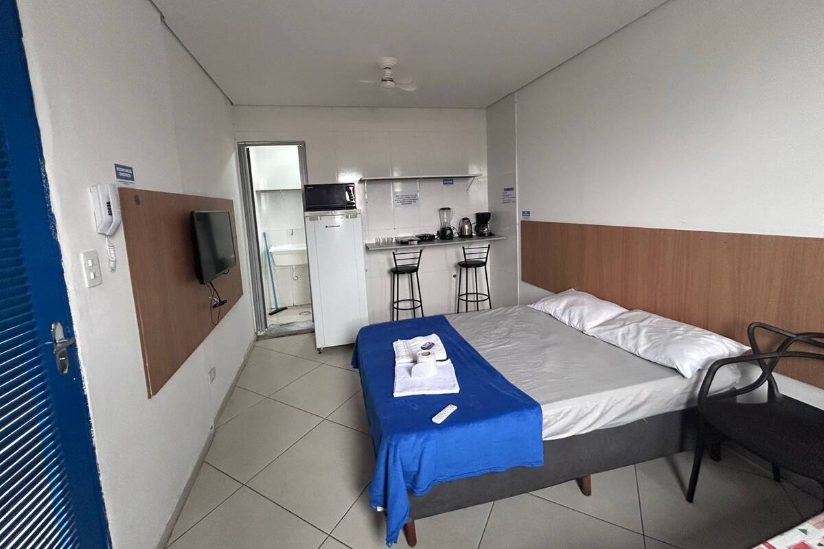 A compact hotel room with a bed, a small desk with a chair, a microwave, and a coffee maker.