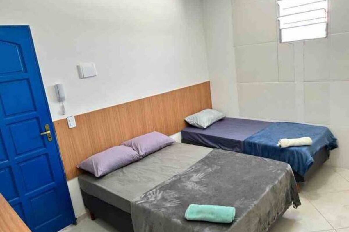 A room with two beds, a blue door, and a window with blinds.