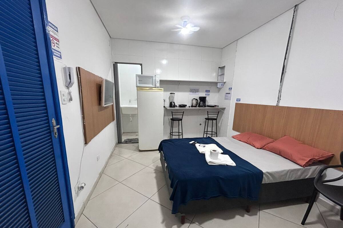 A small, compact room with a bed, a desk, and a kitchenette.