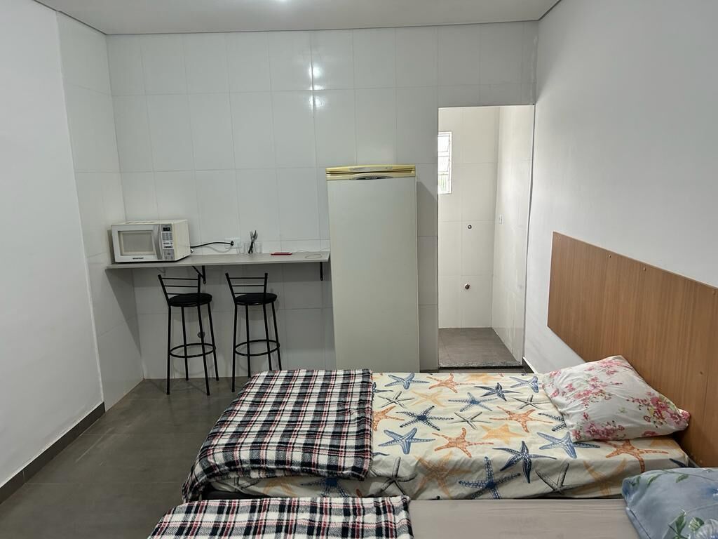 A small, compact room with a bed, a desk with a microwave, two chairs, and a wardrobe.