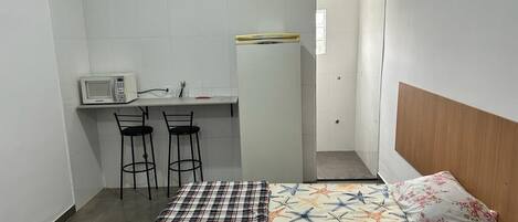 A small, compact room with a bed, a desk with a microwave, two chairs, and a wardrobe.