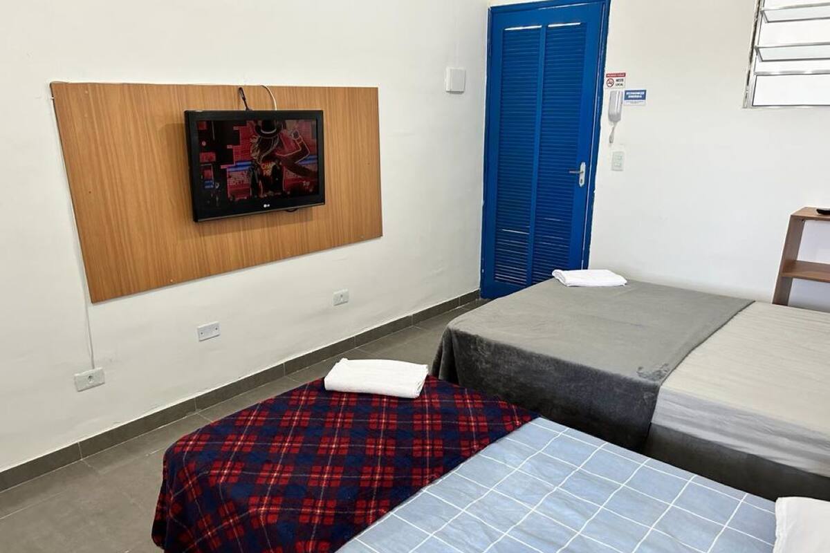 A room with two beds, a wooden panel with a picture, a blue door, and a white wall with a sign.
