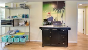 A kitchen with a metal shelving unit, a black cabinet, and a wall mural of a ship. - Pet-friendly Freeport Vacation Rental w/ Deck! (Freeport)