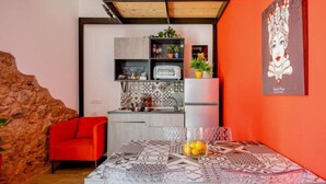 Cuina compacta amb electrodomèstics moderns, zona de menjador amb estovell amb dibuixos i una paret vermella que destaca.