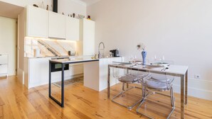 Une cuisine moderne dotée d’un plan de travail en marbre, de meubles blancs et d’un coin repas avec une table en verre et des chaises en métal.