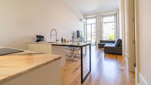 Une cuisine moderne avec un plan de travail en marbre, un coin repas doté d’une table en verre et un canapé gris dans un espace de vie lumineux, agrémenté de parquet et de grandes fenêtres.