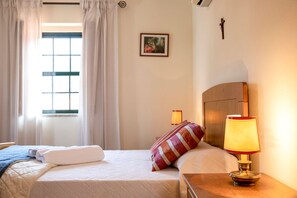 A hotel room with a bed, a nightstand with a lamp, a window with curtains, and a wall-mounted picture.