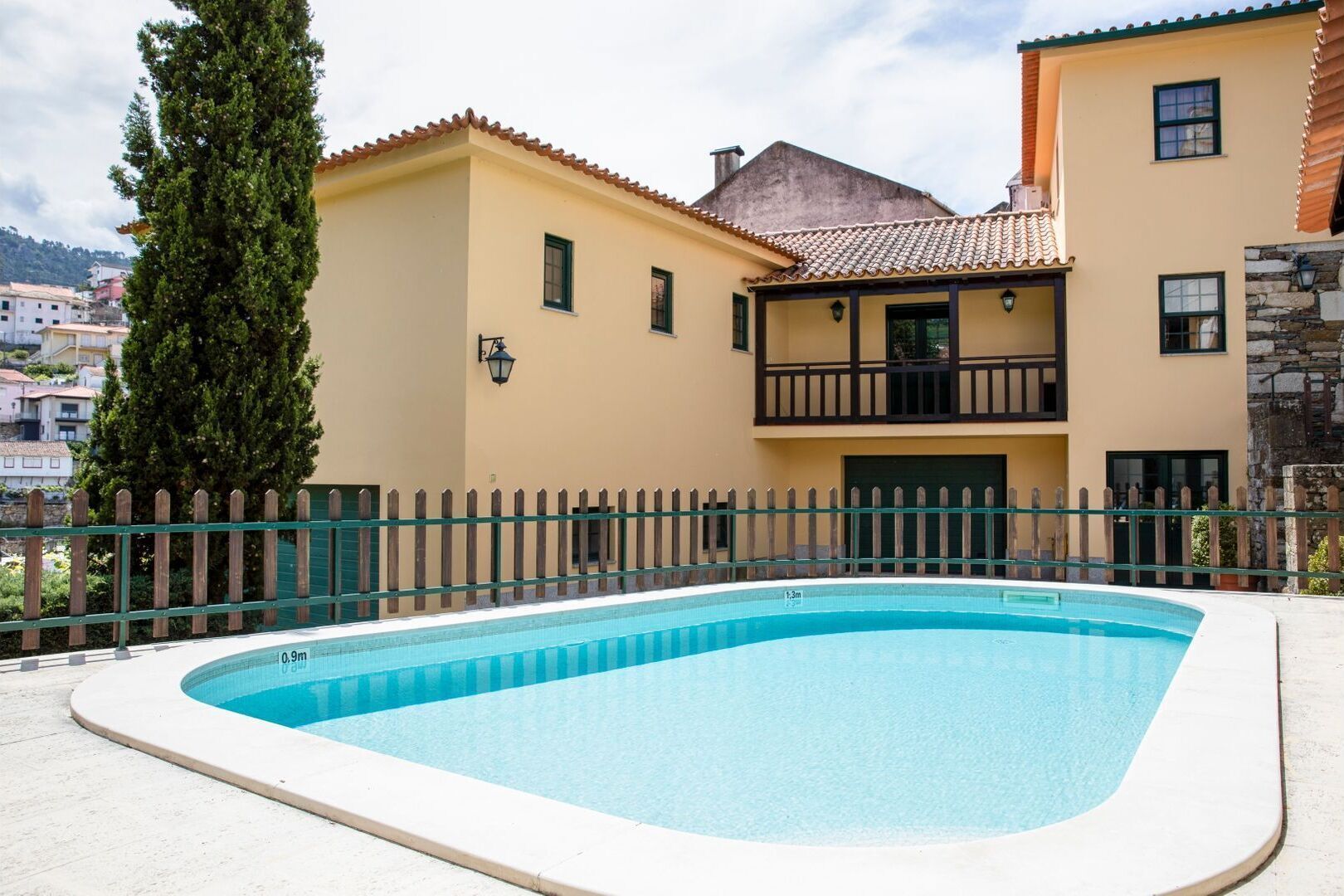 Una piscina con cerramiento de madera, un balcón y un muro de piedra.