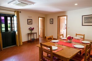 A dining area with a wooden table set for four, a vase of flowers, and a framed picture on the wall.