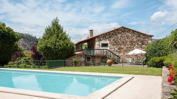 Ein Steinhaus mit Pool, umgeben von viel Grün und Hügeln.