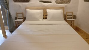 A bed with white linens, wooden headboard, and two nightstands with chairs.