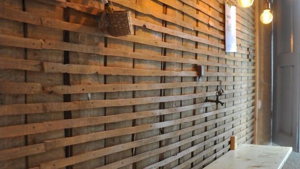 A wooden wall with horizontal planks, a chalkboard menu, hanging light bulbs, and a wooden bench.