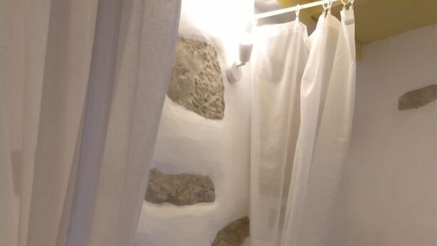 Un lit avec une literie blanche, une chaise et un mur en pierre.
