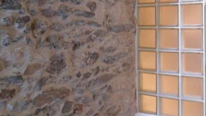 Un mur de pierres surmonté d’un panneau indiquant le mot « AMOUR », une fenêtre à vitres dépolies et un banc en bois.