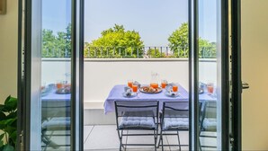 Un balcón con una mesa lista para el desayuno, con platos, vasos y una jarrón.