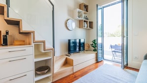 Una sala moderna con una escalera, un televisor de pantalla plana, estanterías de madera y un ventanal corredero que da a un área exterior.