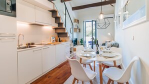 Una cocina moderna con armarios blancos, horno empotrado y comedor con mesa redonda y sillas blancas.