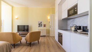 Ein gemütlicher, kleiner Wohnraum mit Küchenzeile, Fernseher und zwei gemusterten Sesseln.