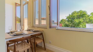 Ein Essbereich mit einem Tisch für vier Personen, zwei Stühlen und einem Fenster mit Blick auf Grünflächen und Gebäude.