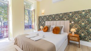 Un dormitorio con una cama grande, dos mesitas de noche, un ventanal con vistas a árboles y un papel tapiz con motivos florales.
