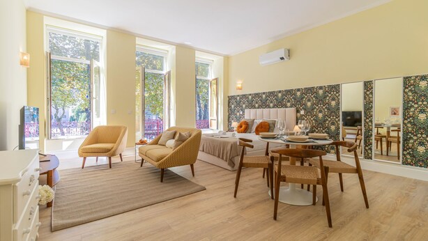 Amplia habitación con una cama grande, dos sillones, una mesa de comedor con sillas y un espejo grande.