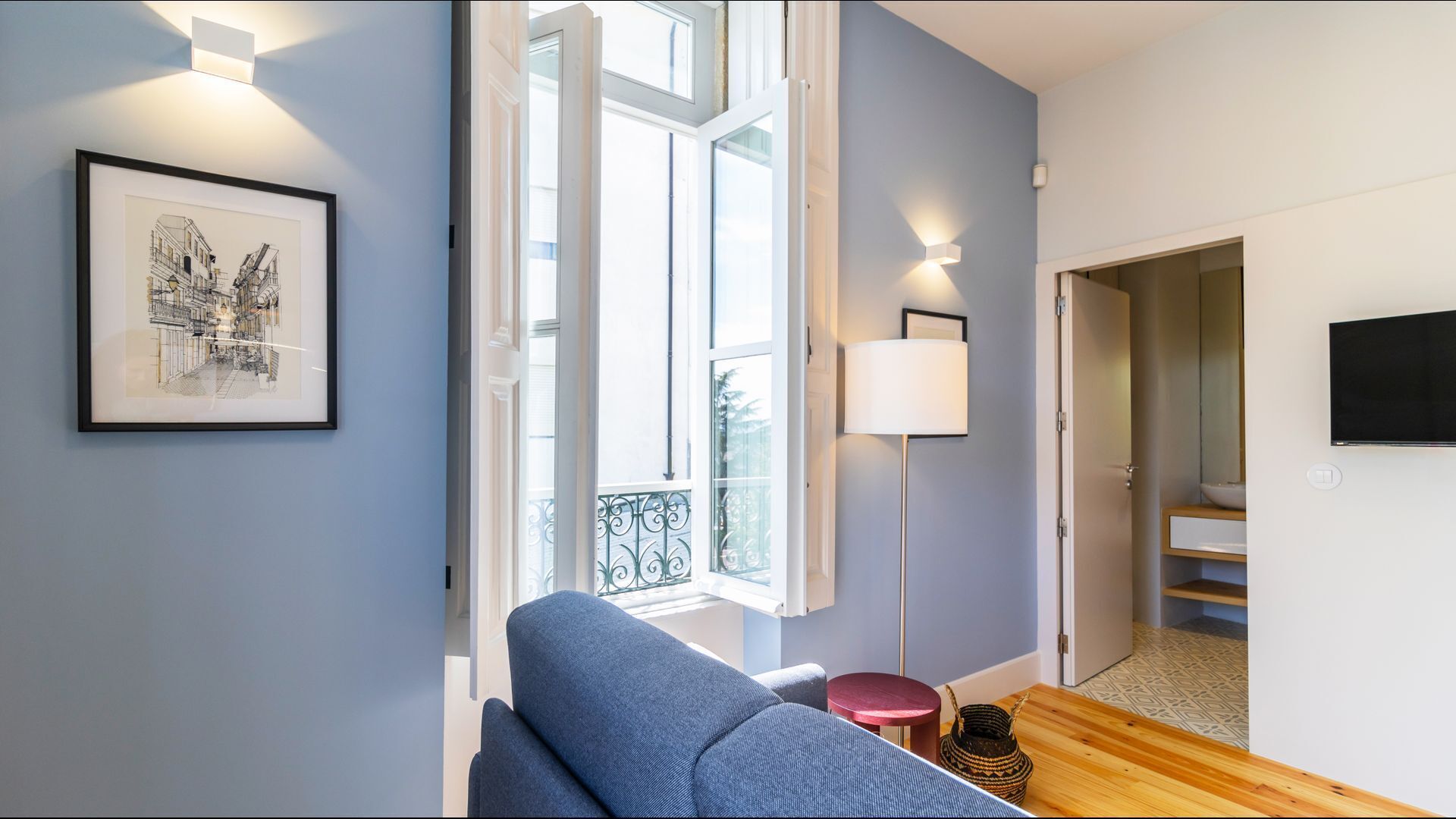 Un salon moderne avec un canapé bleu, une œuvre d’art encadrée, une lampe sur pied et un téléviseur fixé au mur.