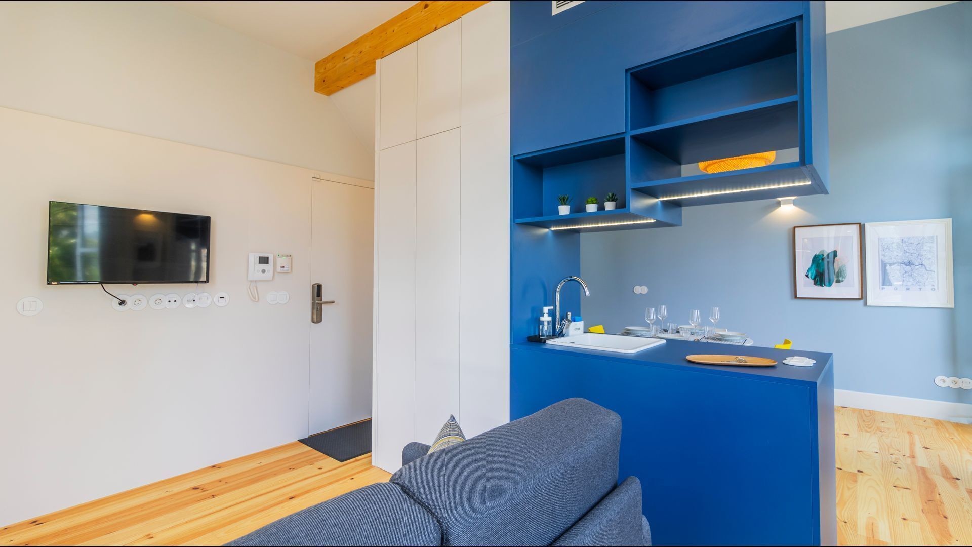 A modern kitchen with a blue accent wall, a built-in sink, and a flat-screen TV mounted on the wall.