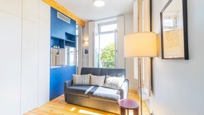 A modern living room with a grey sofa, a small round table, and a blue accent wall. - Barros Lima 493: Apt 2 by LovelyStay (Porto)