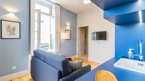 A modern living room with a sofa, a TV mounted on the wall, and a bathroom with a sink and mirror. - Barros Lima 493: Apt 2 by LovelyStay (Porto)