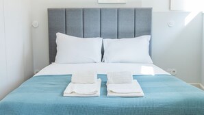 Una cama bien hecha con un cabecero tapizado en gris, almohadas blancas y una colcha azul.