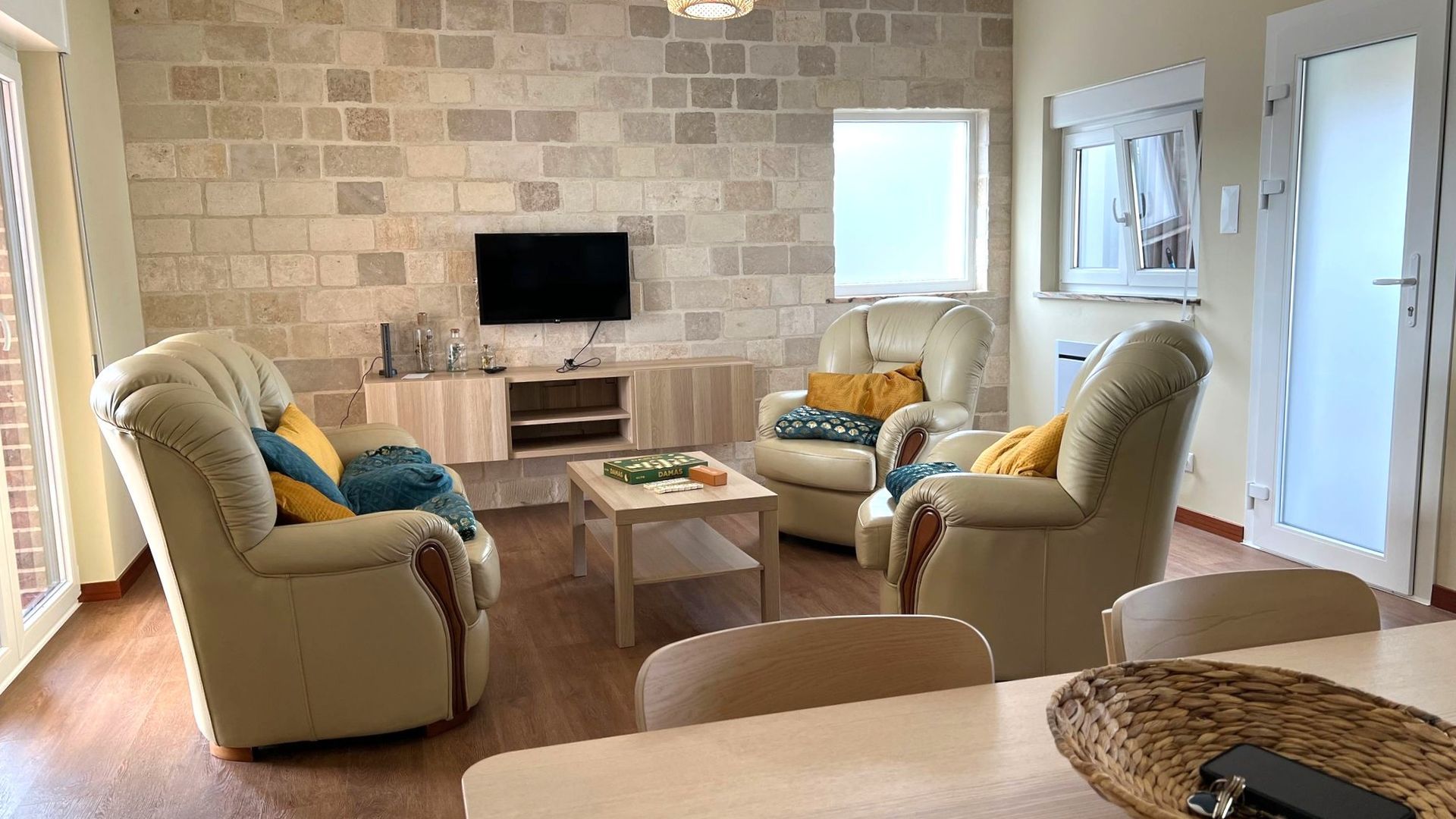 A living room with two leather armchairs, a coffee table, and a flat-screen TV mounted on a stone wall.