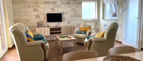 A living room with two leather armchairs, a coffee table, and a flat-screen TV mounted on a stone wall.