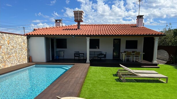 A house with a swimming pool, a deck, and a lawn with lounge chairs.