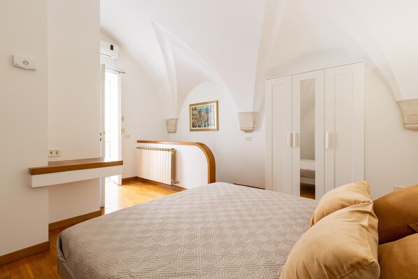 A bedroom with a bed, a wooden headboard, a radiator, a white wardrobe, and a painting on the wall.