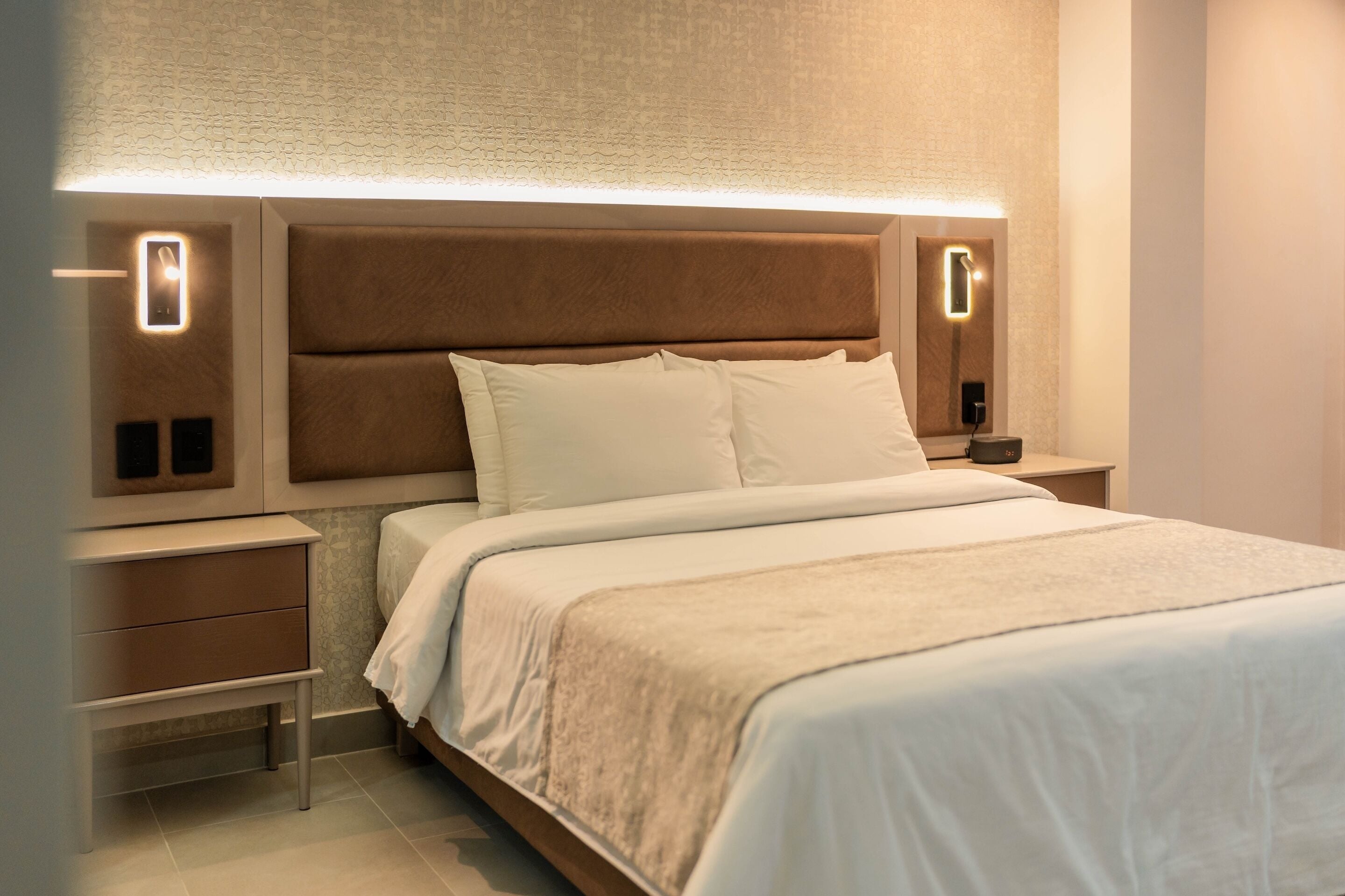 Habitación de hotel moderna con una cama grande, dos mesitas de noche y un cabecero con iluminación integrada.
