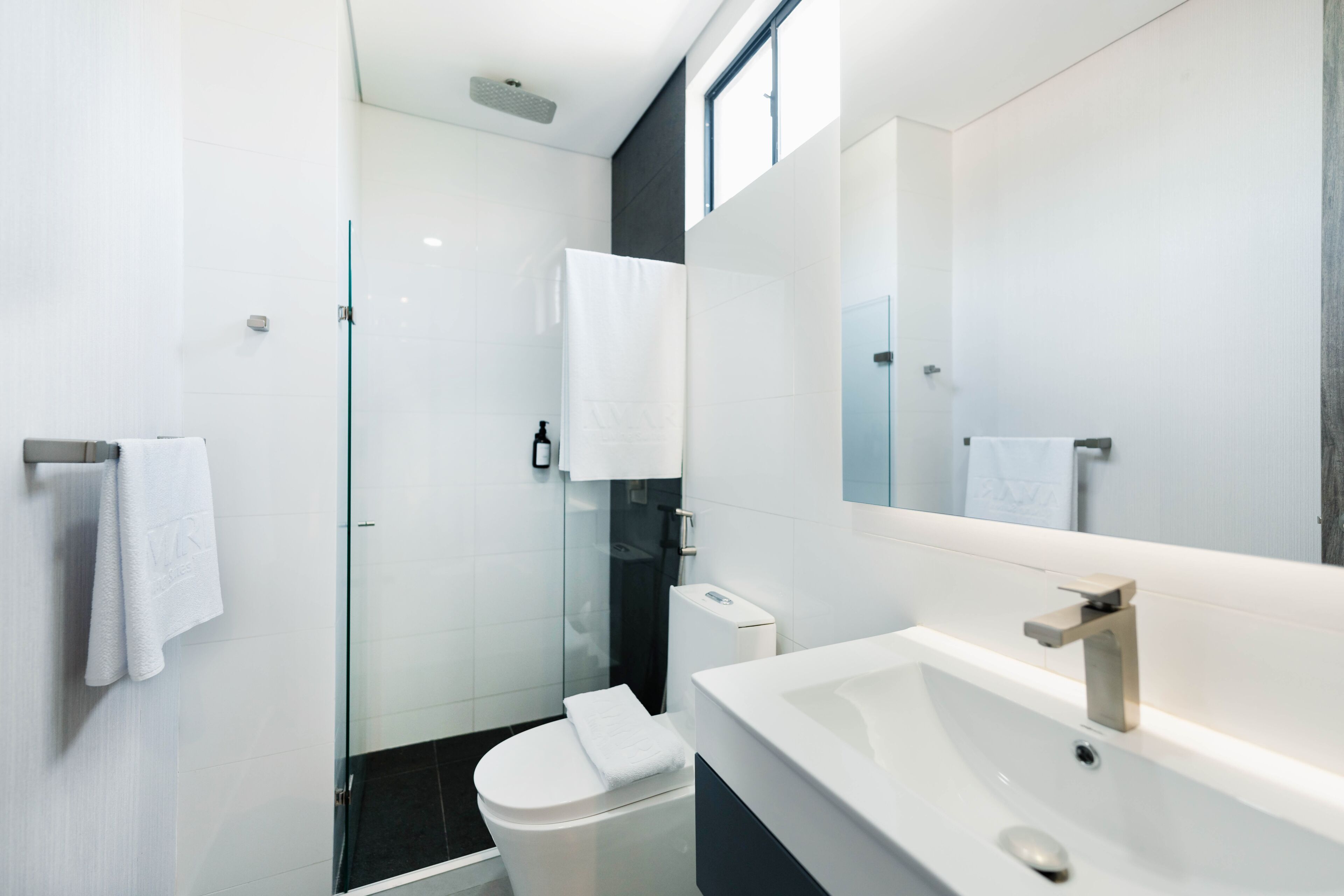 Un baño moderno con cabina de ducha de vidrio, inodoro blanco y un espejo grande sobre un lavamanos blanco.