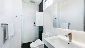 Ein modernes Badezimmer mit Duschkabine aus Glas, einer weißen Toilette und einem großen Spiegel über einem weißen Waschbecken.