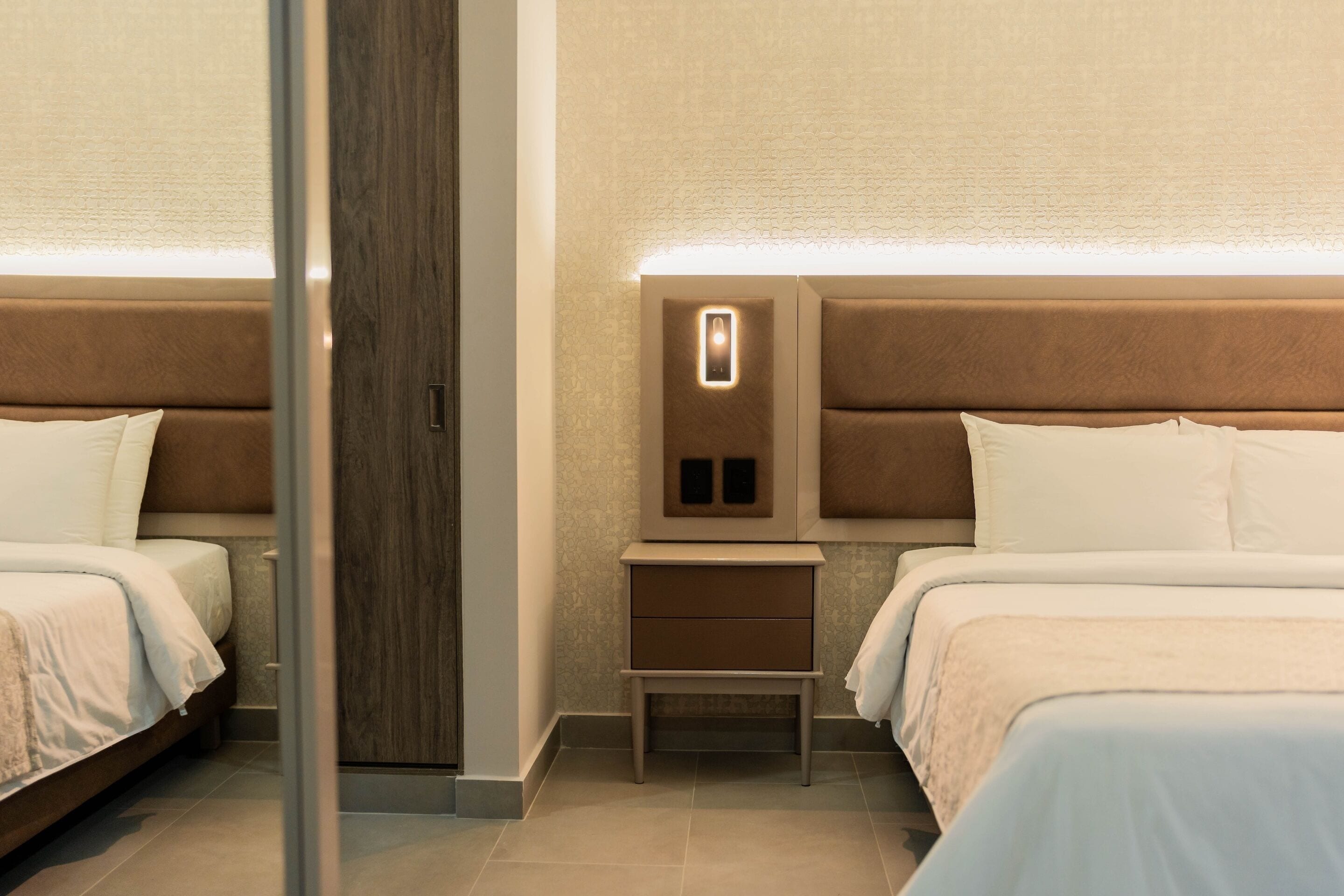 Una habitación de hotel con dos camas, una mesita de noche y una lámpara fijada a la pared.