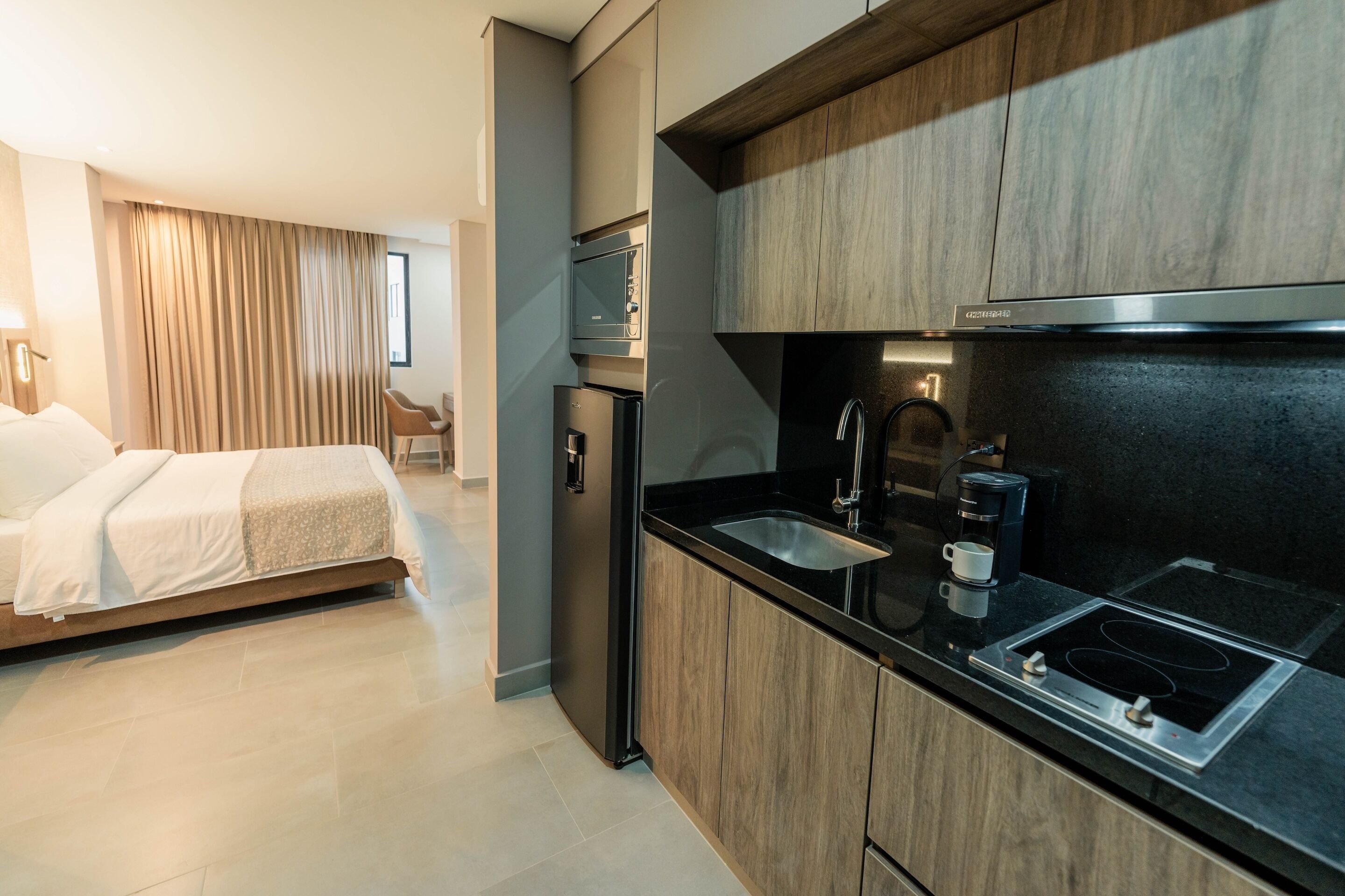 A modern hotel room with a kitchenette, including a microwave, refrigerator, and stove.