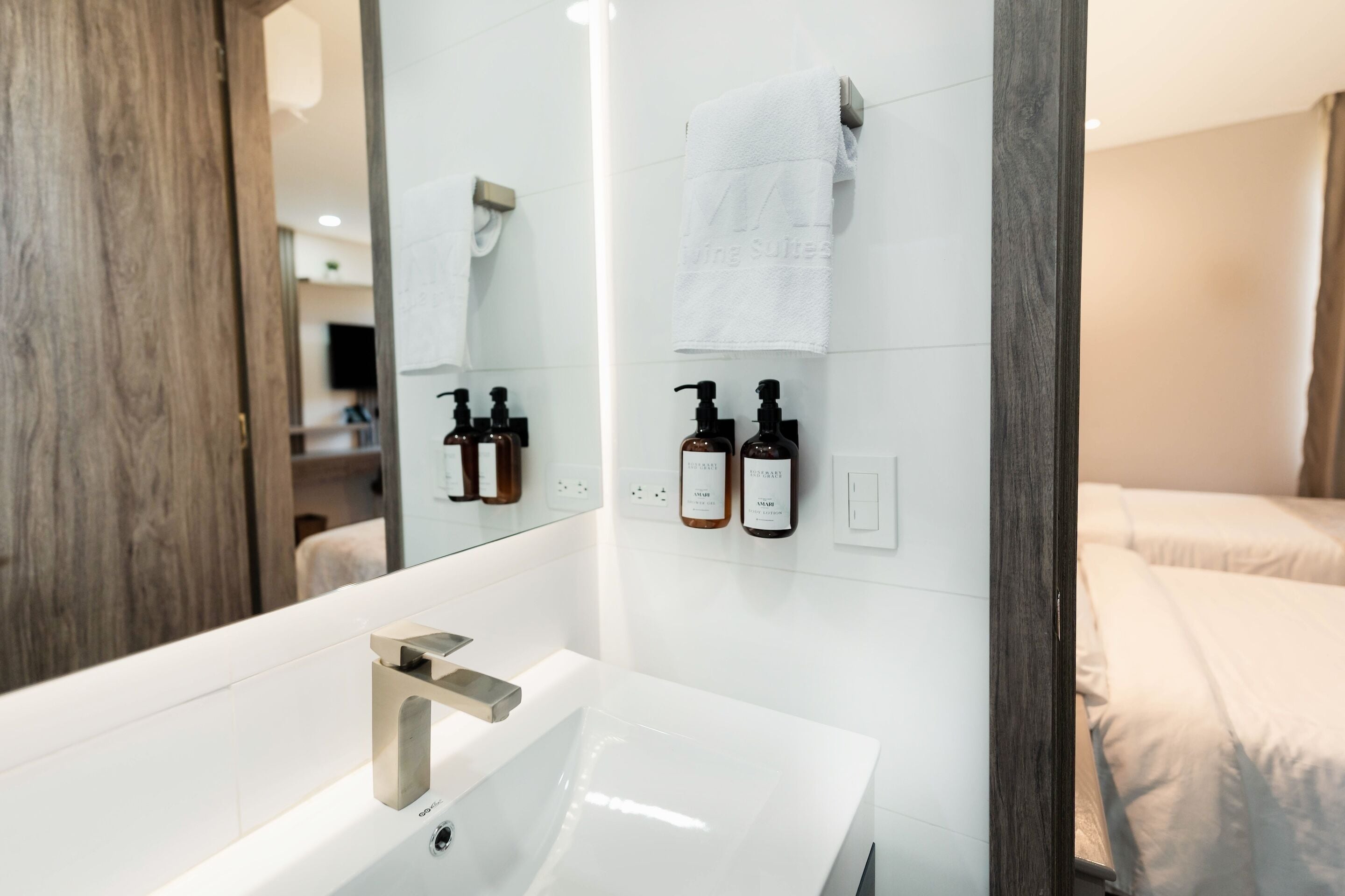 A modern bathroom with a large mirror, a white sink, and two bottles of shampoo and conditioner on the wall.