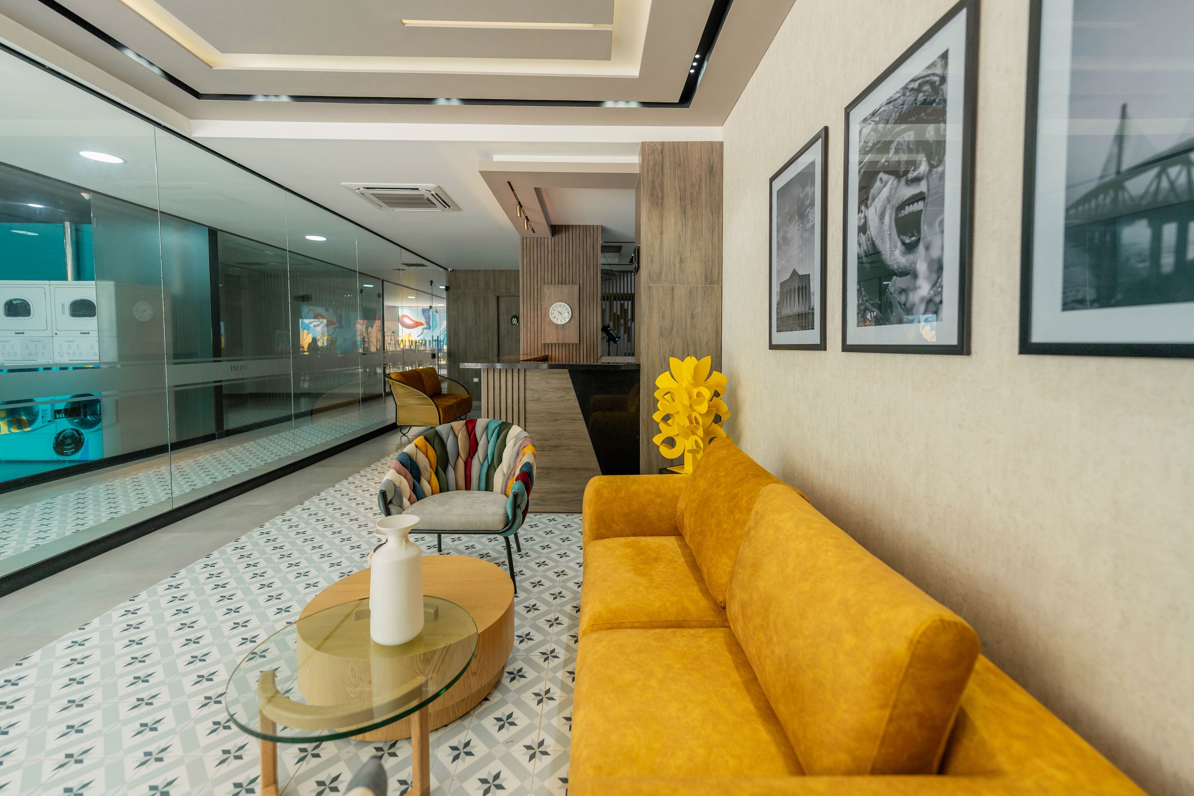 Een moderne lobby met een gele bank, een glazen tafel en een vloer met een patroon.