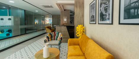 A modern lobby with a yellow sofa, a glass table, and a patterned floor.
