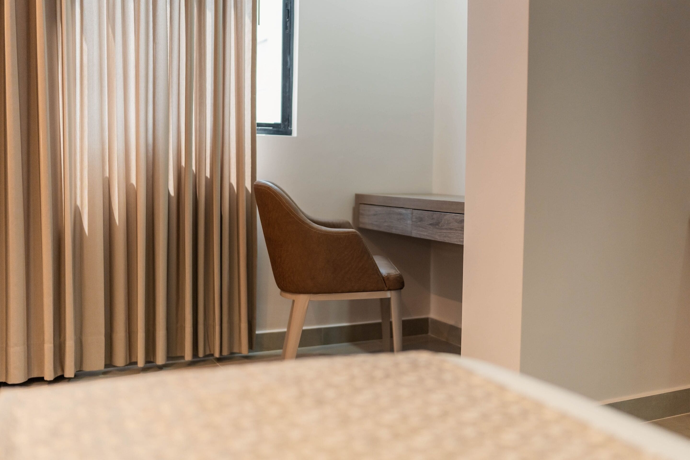 Quarto com cama, cadeira, escrivaninha e janela com cortinas.