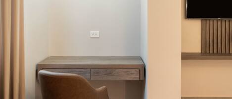 A modern room with a wooden desk, a brown chair, a flat-screen TV mounted on the wall, and a power outlet on the wall.