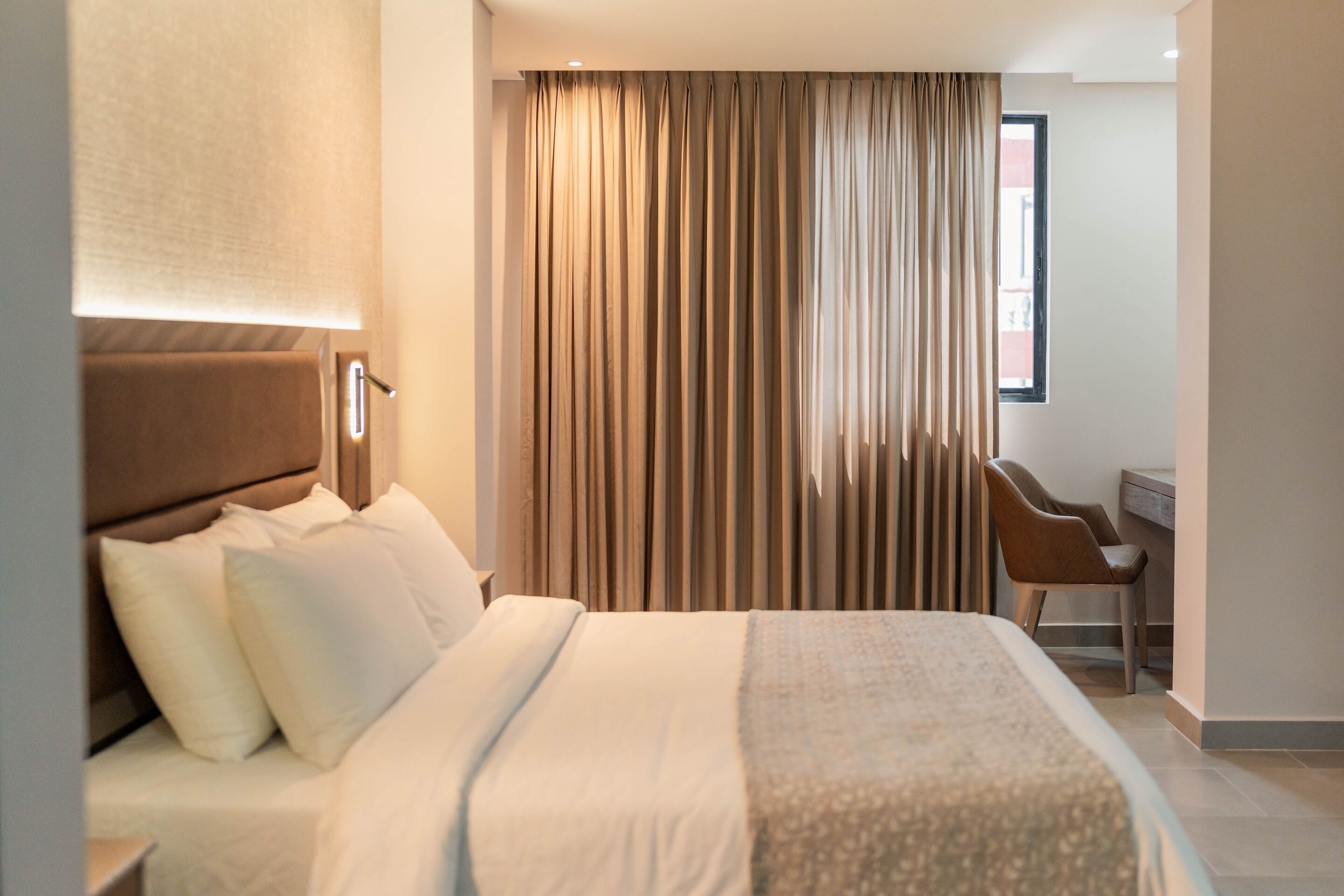 A modern hotel room with a large bed, a desk, and a chair.