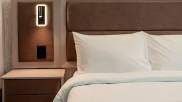 A neatly made bed with white linens and a patterned throw, a nightstand with a lamp, and a wall-mounted light fixture.